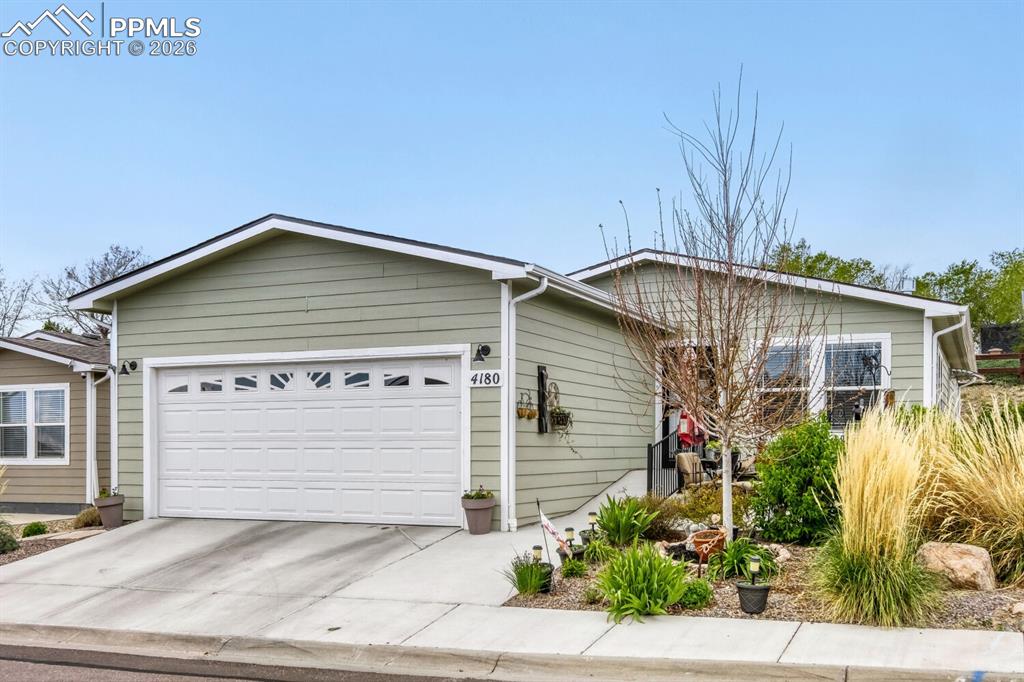 Image 2 of 33: Light green siding exterior with a white two-car garage featuring decorativ