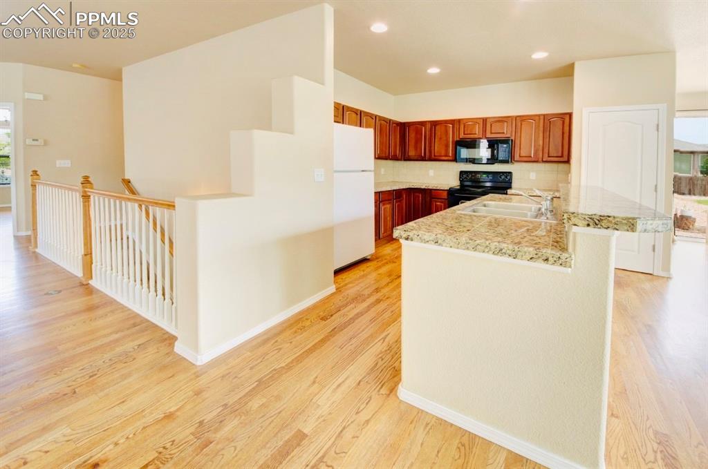 Image 11 of 42: Kitchen with light countertops, light wood-type flooring, black appliances,