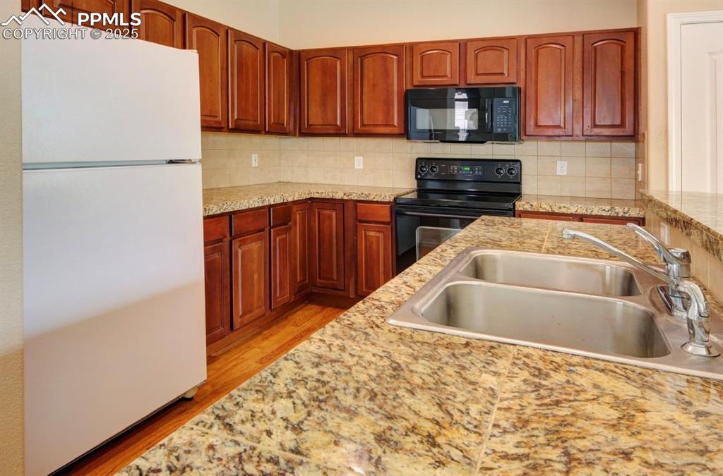 Image 12 of 42: Kitchen with black appliances, tasteful backsplash, brown cabinetry, light 