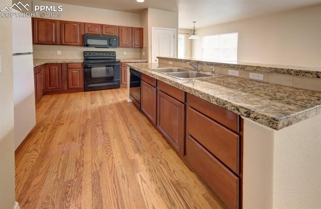 Image 14 of 42: Kitchen with backsplash, black appliances, brown cabinets, and light wood f