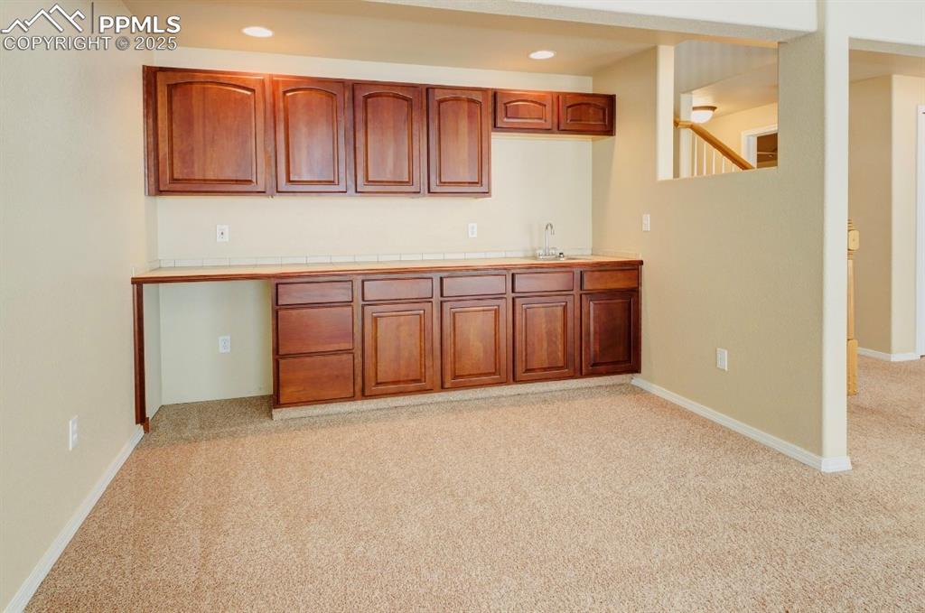 Image 31 of 42: Kitchen with tile counters, light carpet, brown cabinets, and recessed ligh