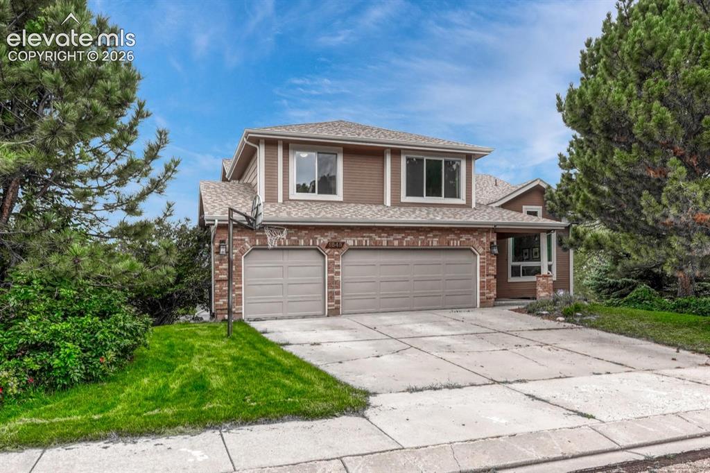 Caption: Two-story residence featuring a three-car garage, brick facade accents, and mature evergreen trees