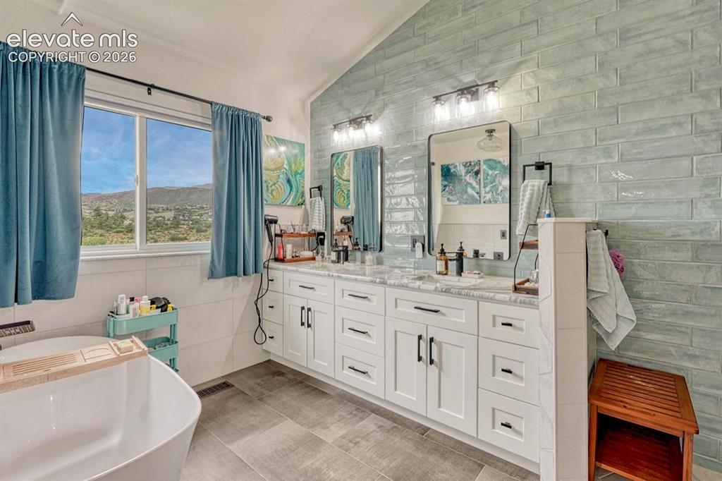Image 21 of 41: Freestanding soaking tub, dual vanity with white cabinetry, tile flooring,