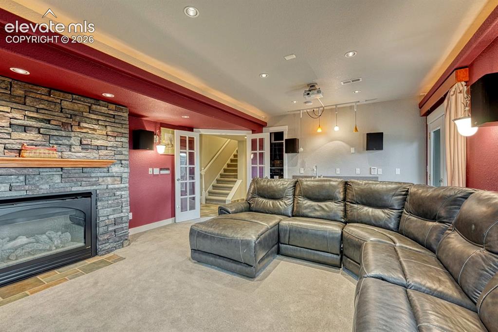 Image 25 of 41: Stone-clad fireplace with mantel, recessed lighting, double French doors, a