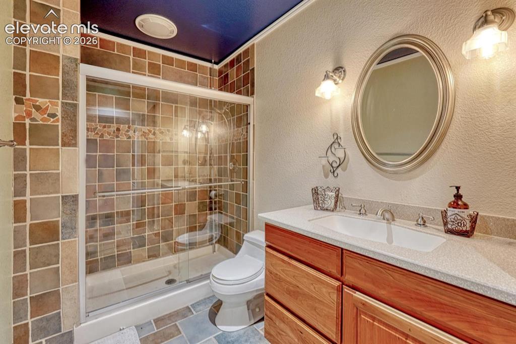 Image 26 of 41: Tiled shower enclosure with sliding glass door, mosaic tile accents, vanity