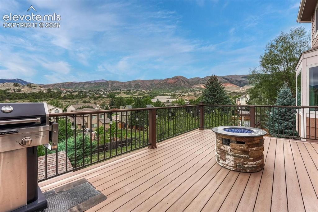 Image 30 of 41: Spacious outdoor deck with composite decking, stone fire pit, and metal rai