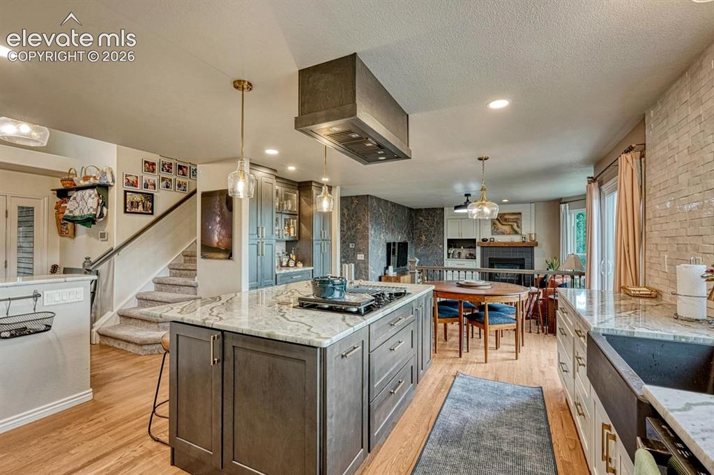 Image 9 of 41: Central kitchen island with cooktop and stone countertop, wood flooring, re