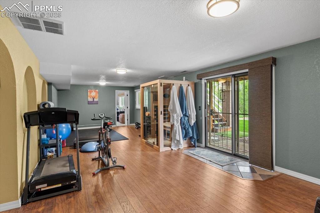 Image 31 of 49: Exercise room with wood finished floors, a textured wall, baseboards, and a