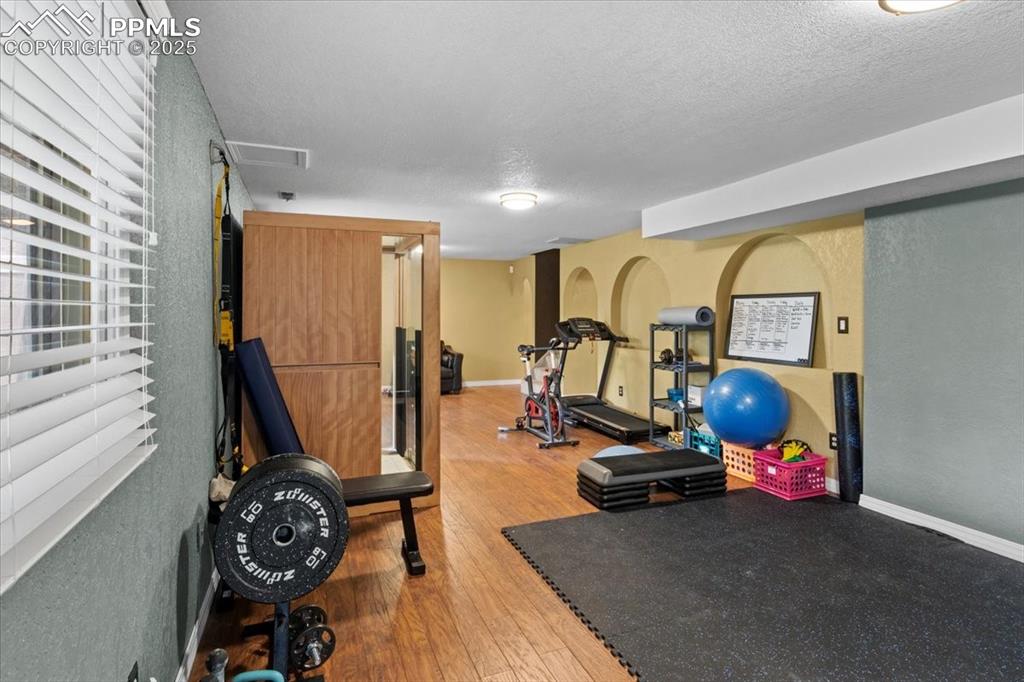 Image 32 of 49: Workout room with wood finished floors, a textured ceiling, and baseboards