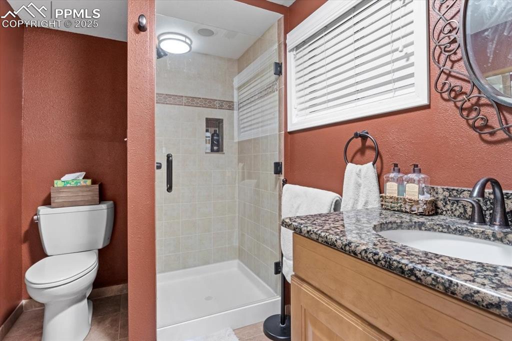 Image 35 of 49: Full bath with a textured wall, a shower stall, toilet, vanity, and tile pa