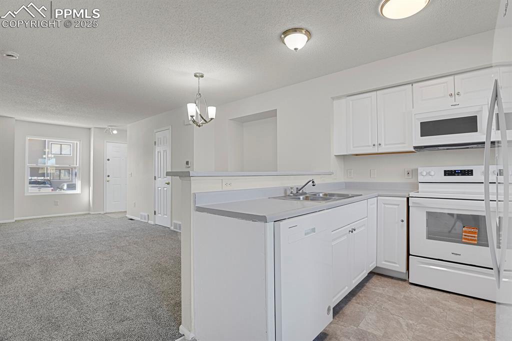 Image 8 of 27: Kitchen with white appliances, open floor plan, a peninsula, a textured cei
