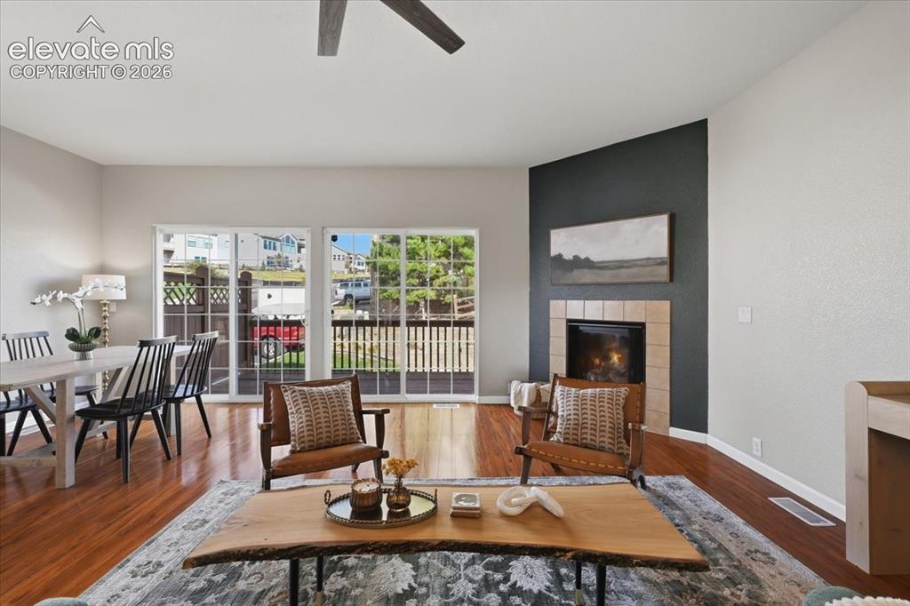 Image 9 of 34: Hardwood flooring, tiled fireplace surround, high ceilings, ceiling fan, an