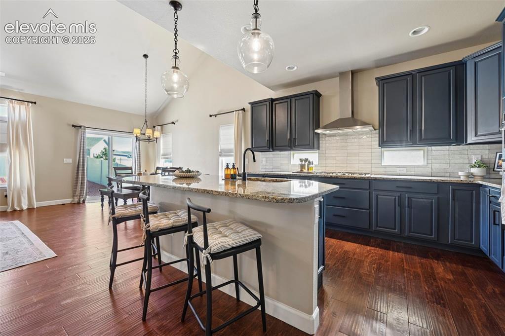 Image 10 of 46: Kitchen featuring wood-finish flooring, dark-toned cabinetry, stone-surface