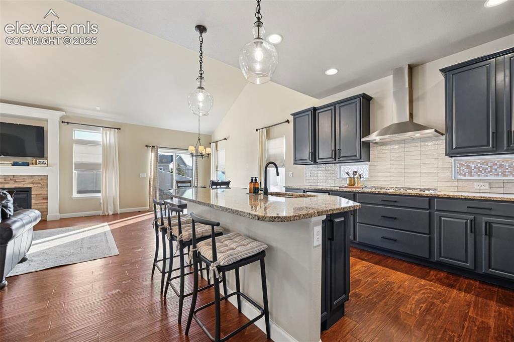 Image 11 of 47: Vaulted ceiling, wood-finish flooring, stone-clad fireplace, kitchen island