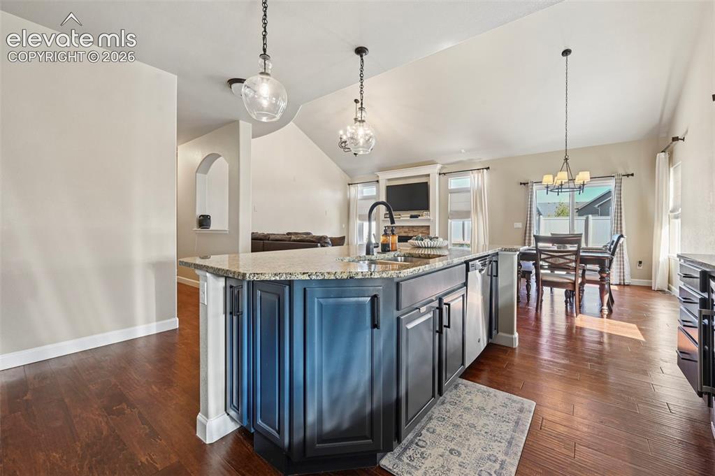 Image 11 of 46: Kitchen island with dark cabinetry, stone countertops, and an undermount si