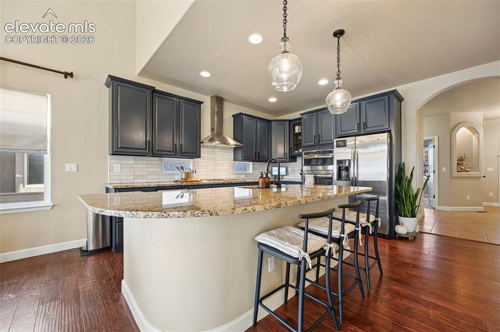 Image 12 of 47: Kitchen featuring a large curved island, stainless steel appliances, dark w