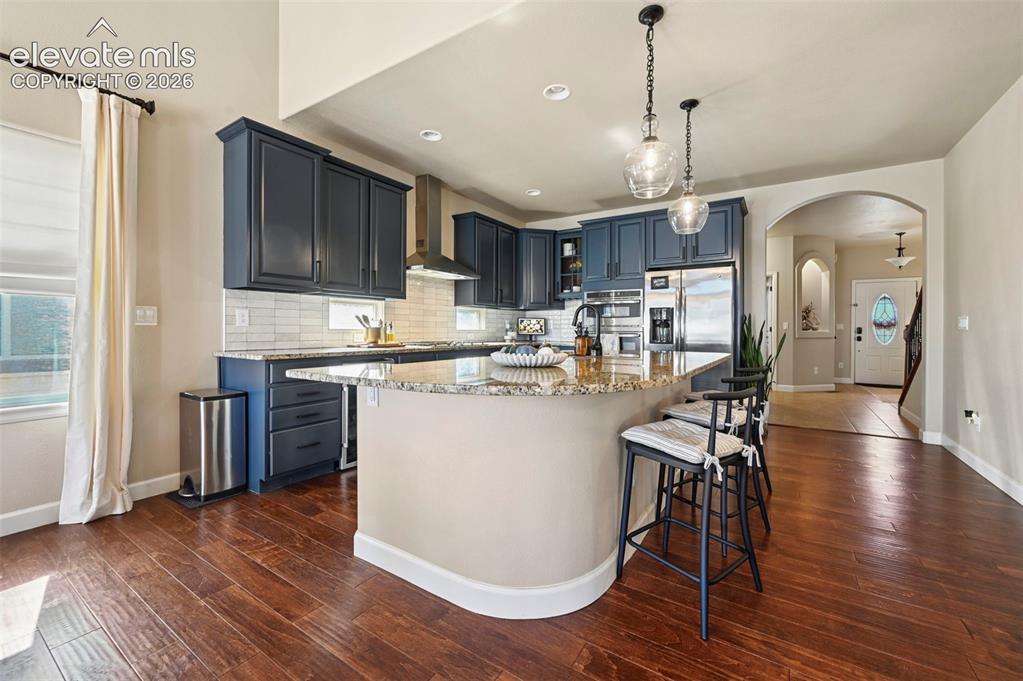 Image 13 of 46: Kitchen featuring dark cabinetry, stone-finish countertops, a central islan