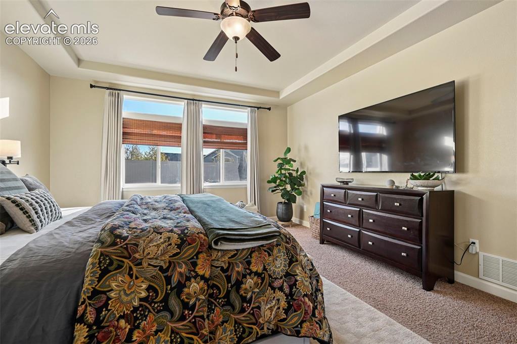 Image 15 of 46: Tray ceiling with a ceiling fan, wall-mounted sconce lighting, and multiple