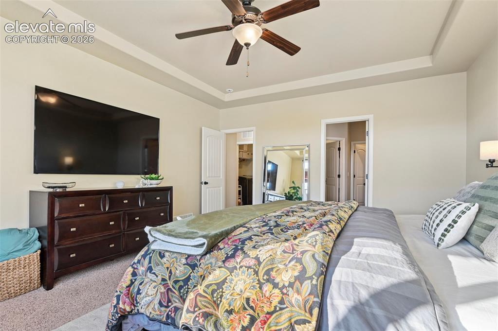 Image 16 of 47: Tray ceiling, ceiling fan with light, wall-mounted television, and sconce l