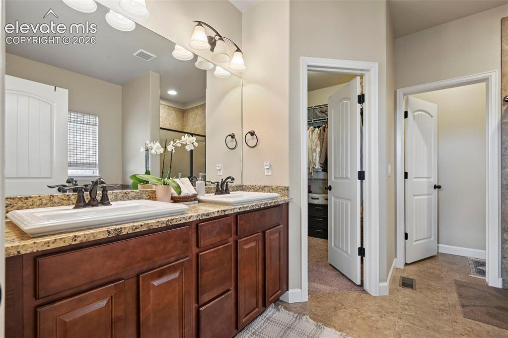 Image 18 of 46: Dual vanities with stone-finish countertops, wood-finish cabinetry, and fra