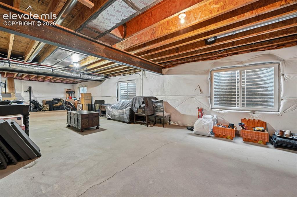 Image 31 of 47: Exposed structural beams, two windows with window wells, concrete flooring,