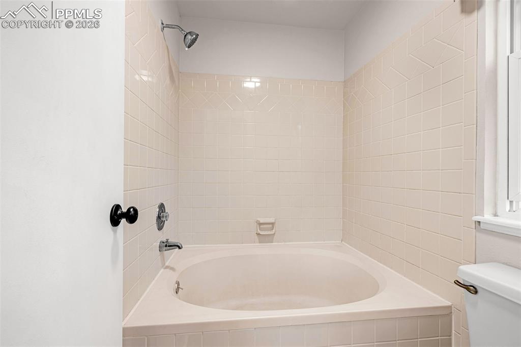 Image 15 of 41: Alcove bathtub with light-colored tile surround and walls