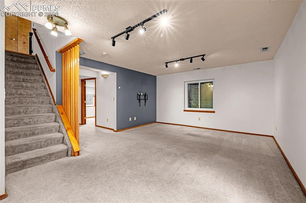 Image 20 of 41: Carpeted room with a staircase featuring wooden railing and a gray accent w