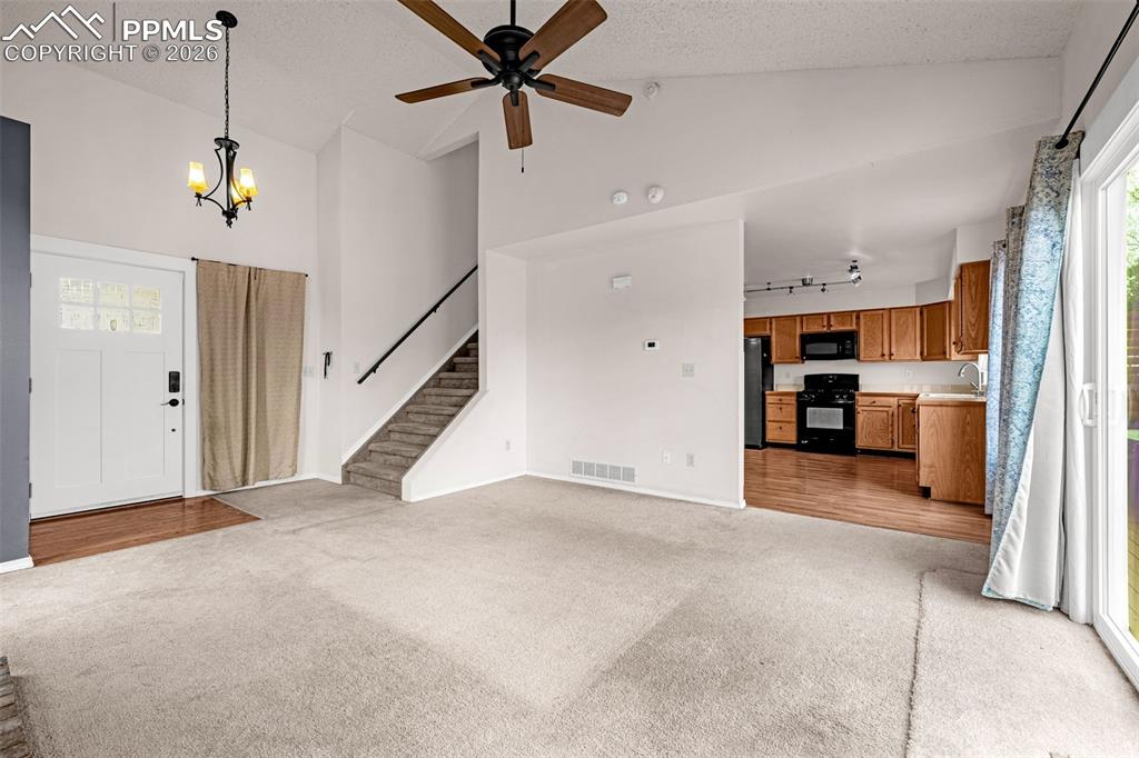 Image 5 of 41: Open-concept living area featuring vaulted ceilings, a ceiling fan, and car