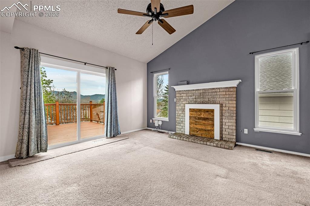 Image 8 of 41: Carpeted room with a vaulted ceiling, a brick fireplace, and sliding glass 