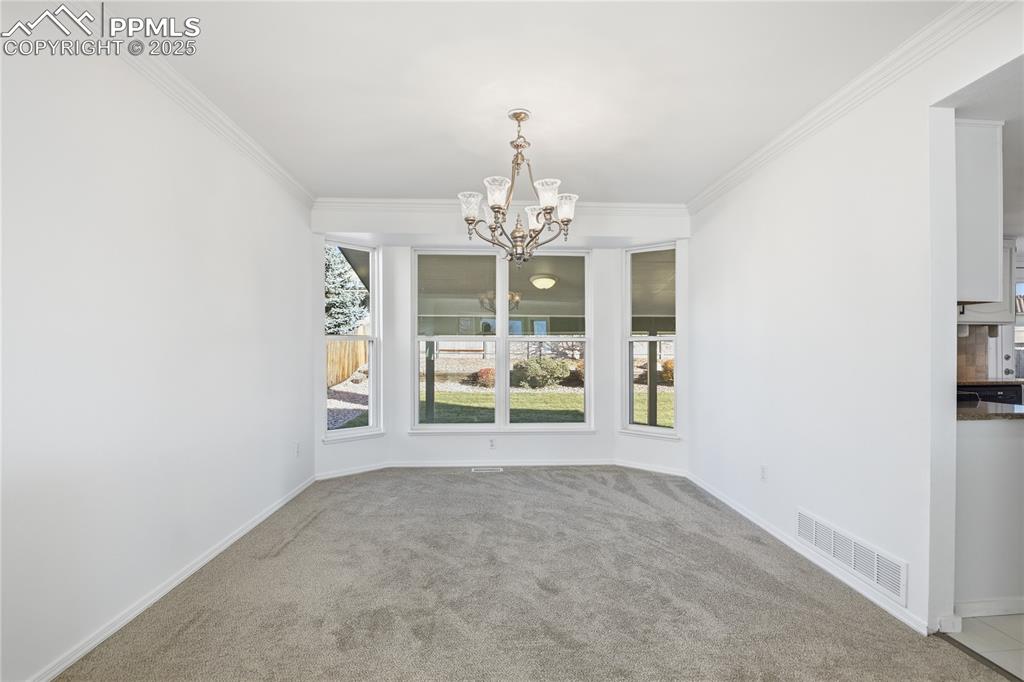 Image 10 of 42: Unfurnished dining area featuring a chandelier, crown molding, and carpet f