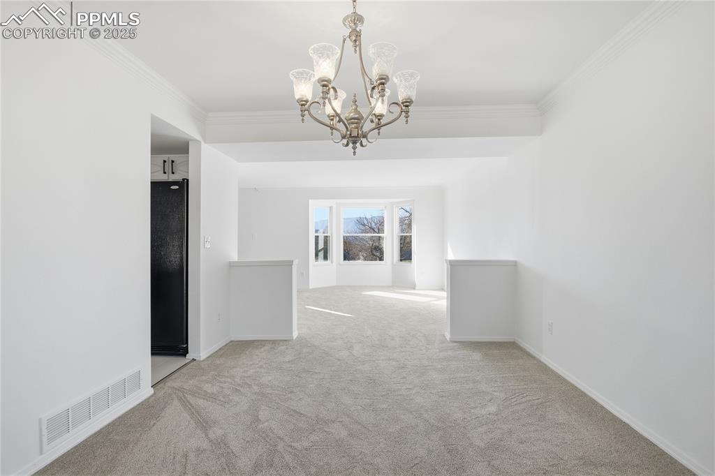 Image 11 of 42: Spare room featuring ornamental molding, light colored carpet, and a chande