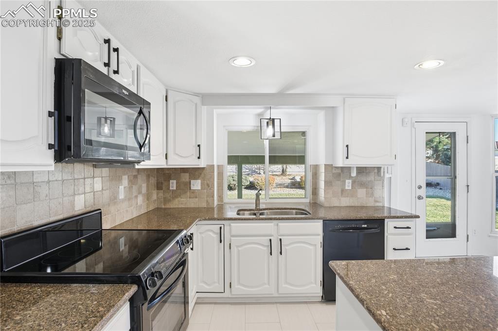 Image 12 of 42: Kitchen featuring black appliances, dark stone countertops, decorative back
