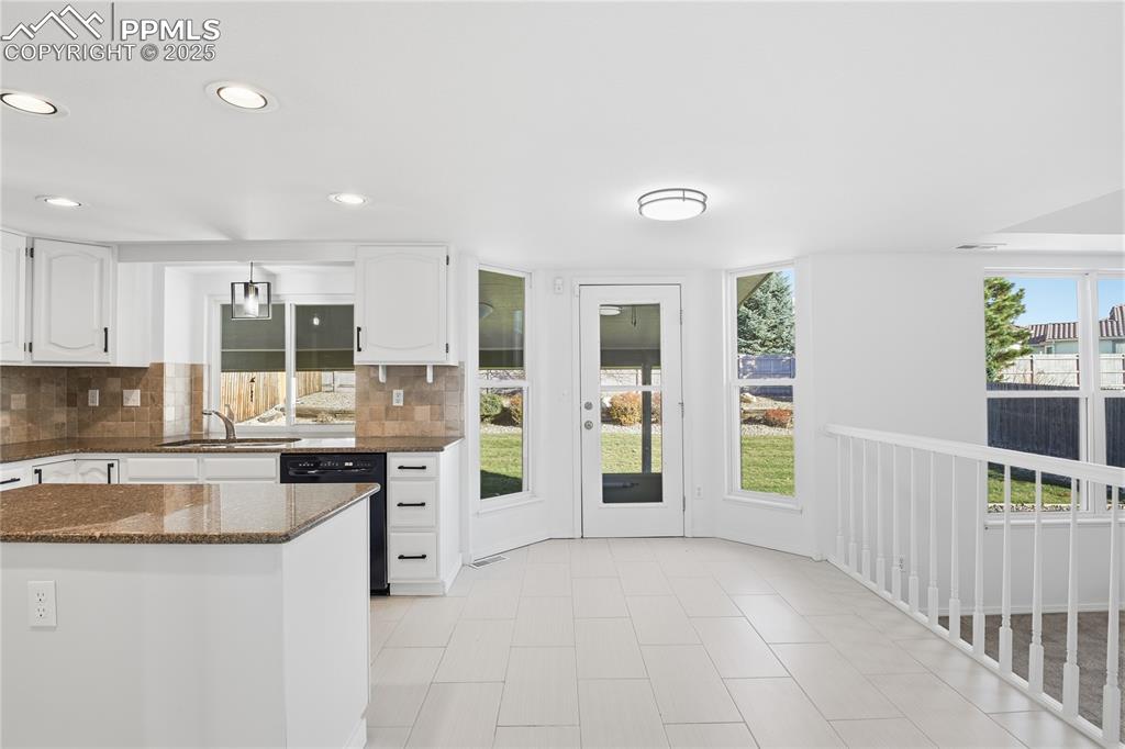 Image 13 of 42: Kitchen with dark stone counters, tasteful backsplash, white cabinets, heal
