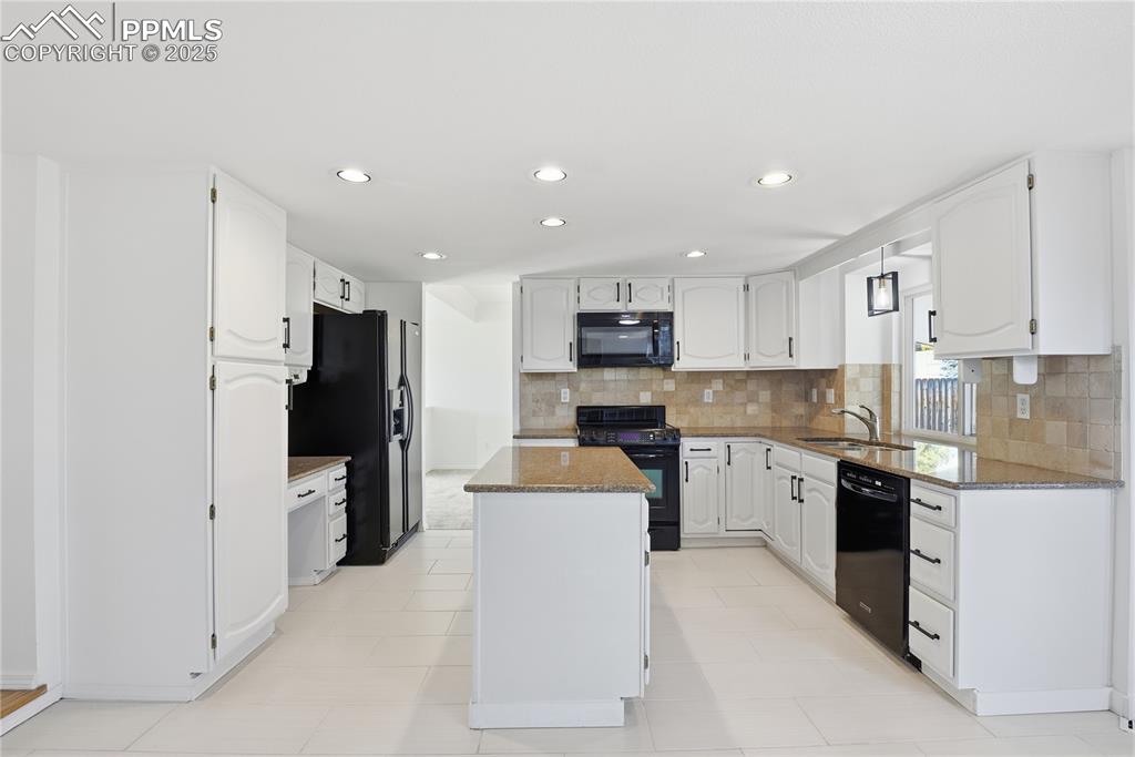 Image 14 of 42: Kitchen featuring dark stone counters, backsplash, black appliances, white 