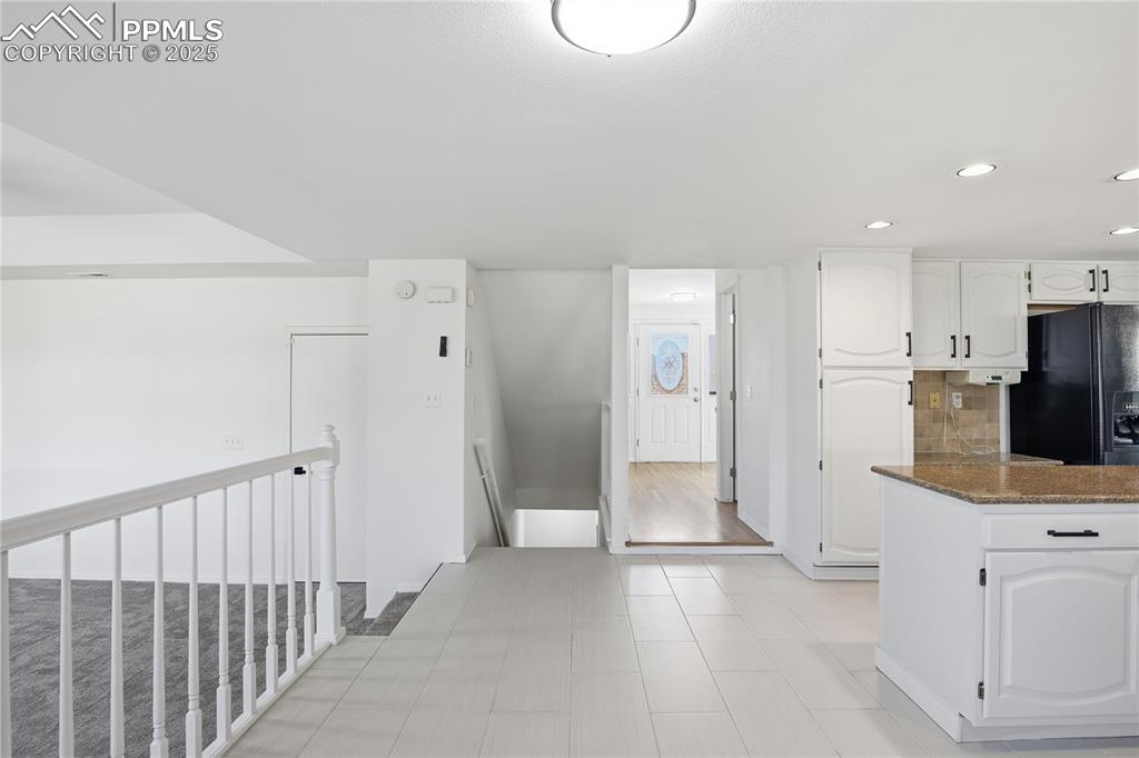 Image 15 of 42: Kitchen with white cabinets, dark stone countertops, black refrigerator wit