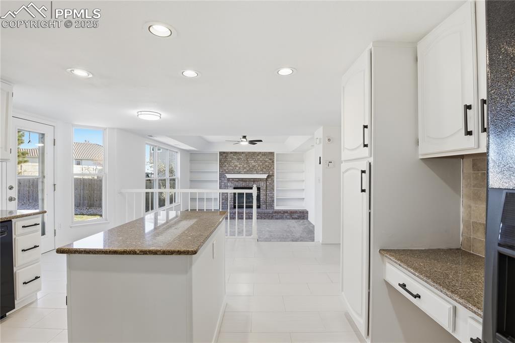 Image 4 of 42: Kitchen featuring a fireplace, white cabinetry, recessed lighting, dark sto