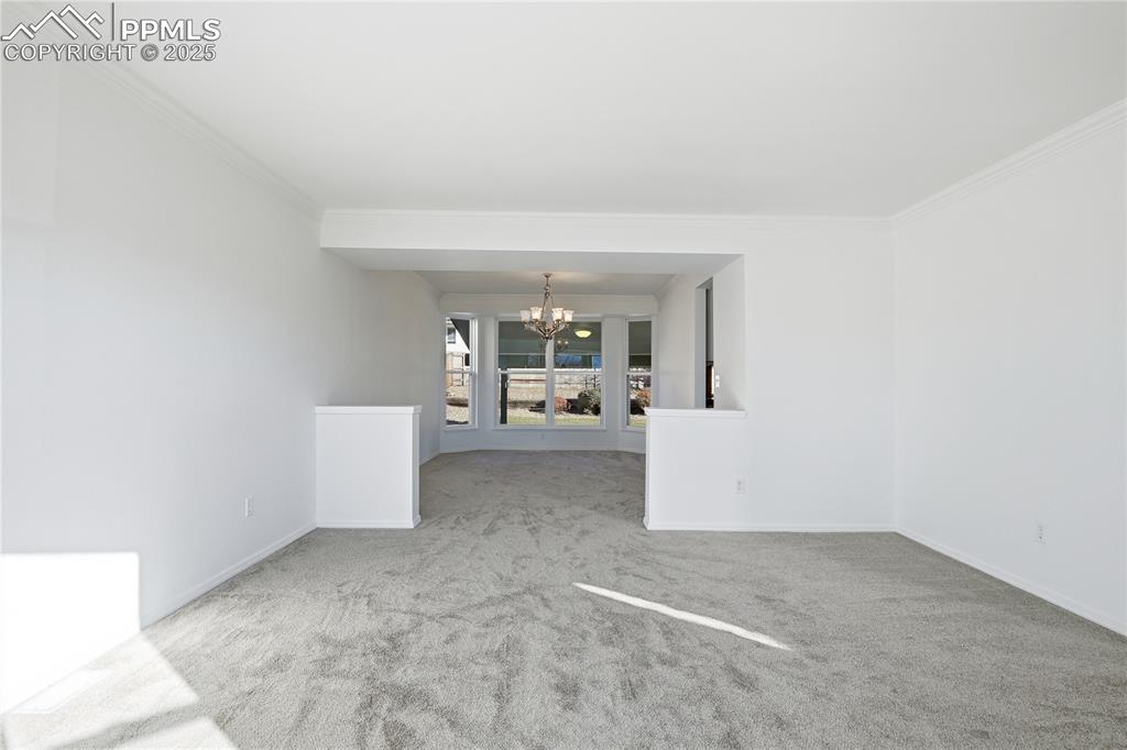 Image 7 of 42: Spare room with a chandelier, light colored carpet, and ornamental molding