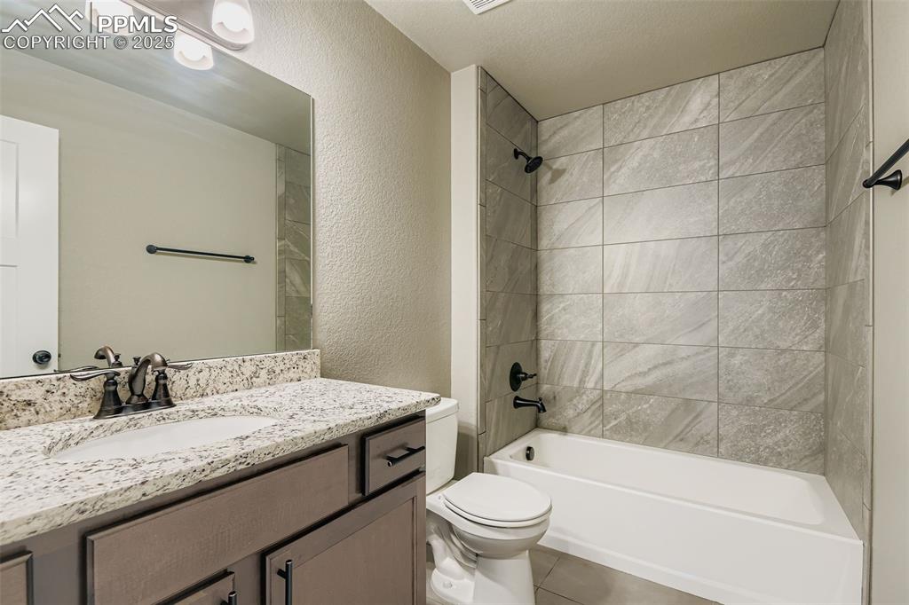 Image 20 of 28: Full bath featuring a textured wall,  shower combination, vanity, and tile 