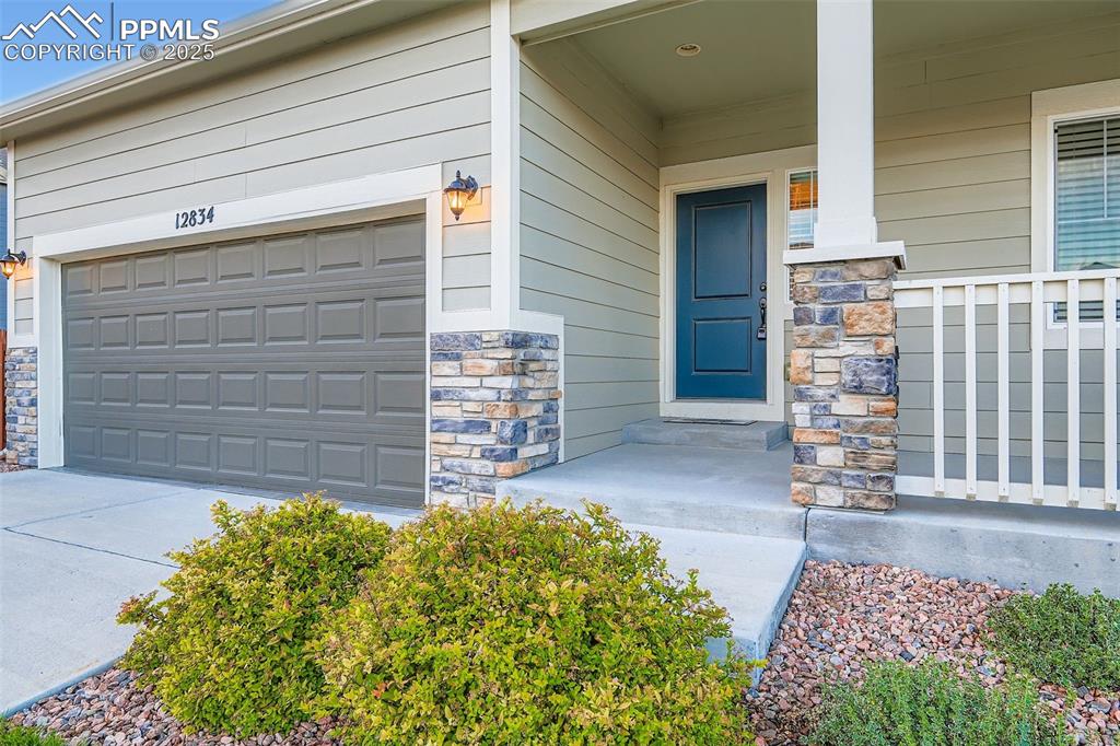 Image 3 of 28: Doorway to property with stone siding, covered porch, and concrete driveway