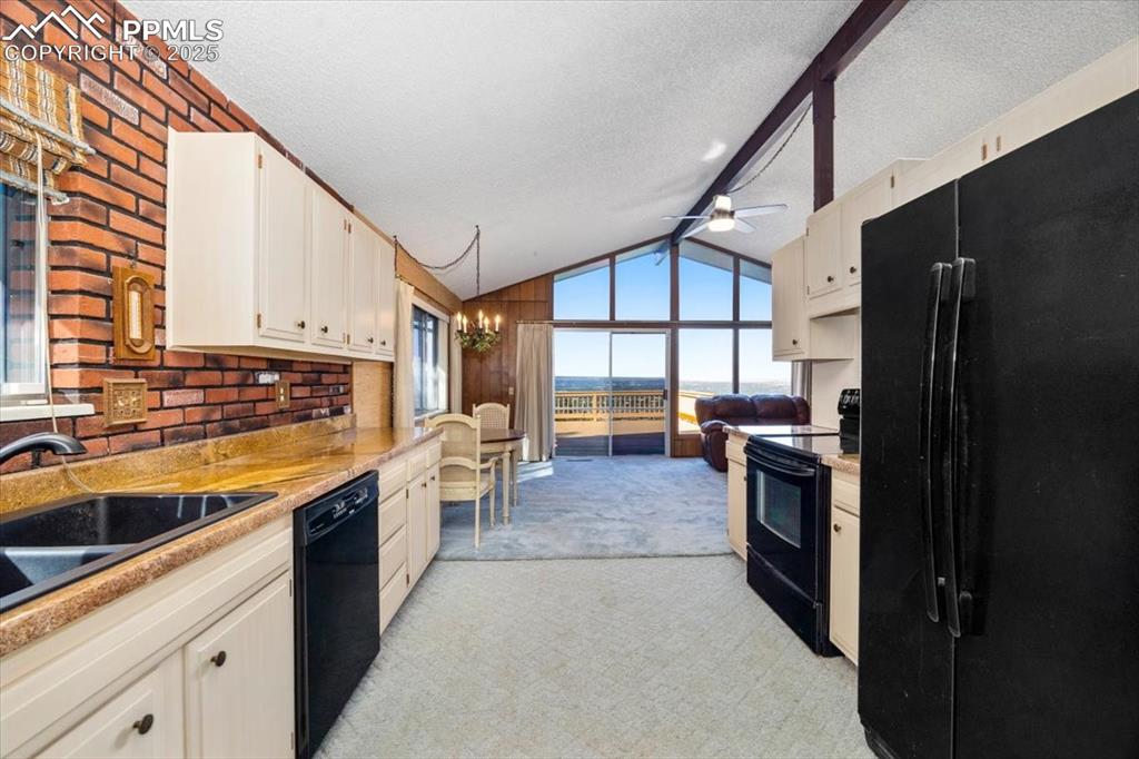 Image 19 of 38: Kitchen with black appliances, light carpet, a textured ceiling, a chandeli
