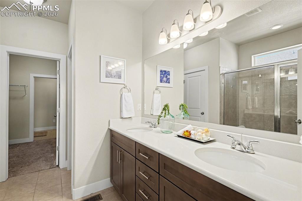 Image 10 of 37: The primary bathroom features dual sinks, a glass-enclosed standing shower,