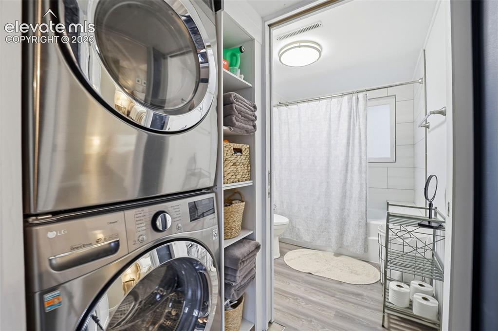 Image 21 of 38: Laundry area featuring a stacked washer and dryer, adjacent to a bathroom w