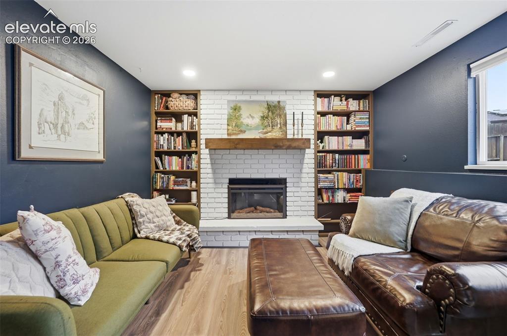 Image 23 of 38: Living space featuring a white brick fireplace with a wood mantle, built-in