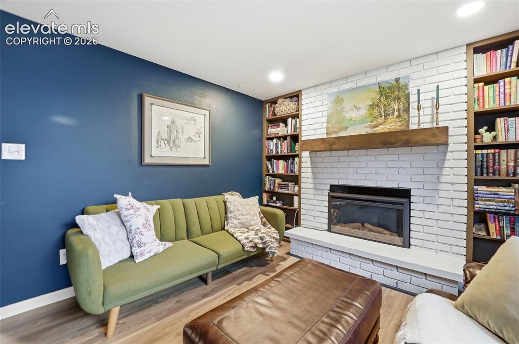 Image 24 of 38: Living area featuring wood-finish flooring, a white brick fireplace with a