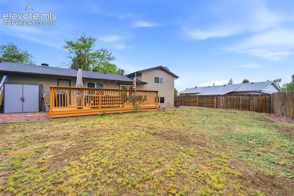 Image 38 of 38: Spacious backyard featuring a large wooden deck, privacy fencing, and a bui