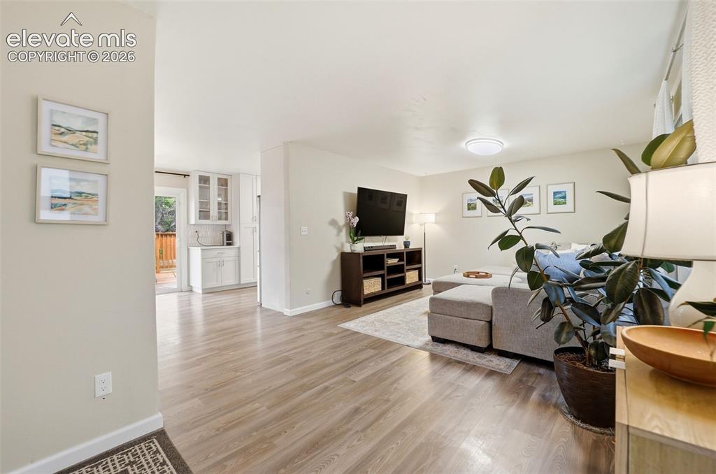 Image 4 of 38: Spacious living area featuring light-toned walls, wood-finish flooring, a f