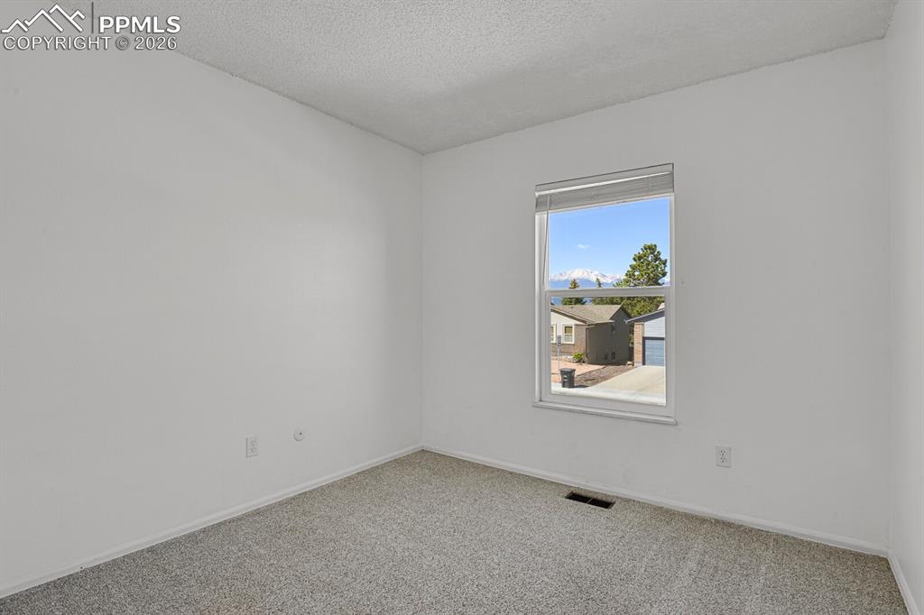 Image 15 of 30: Neutral-toned room featuring a window with views of mountains and trees, li