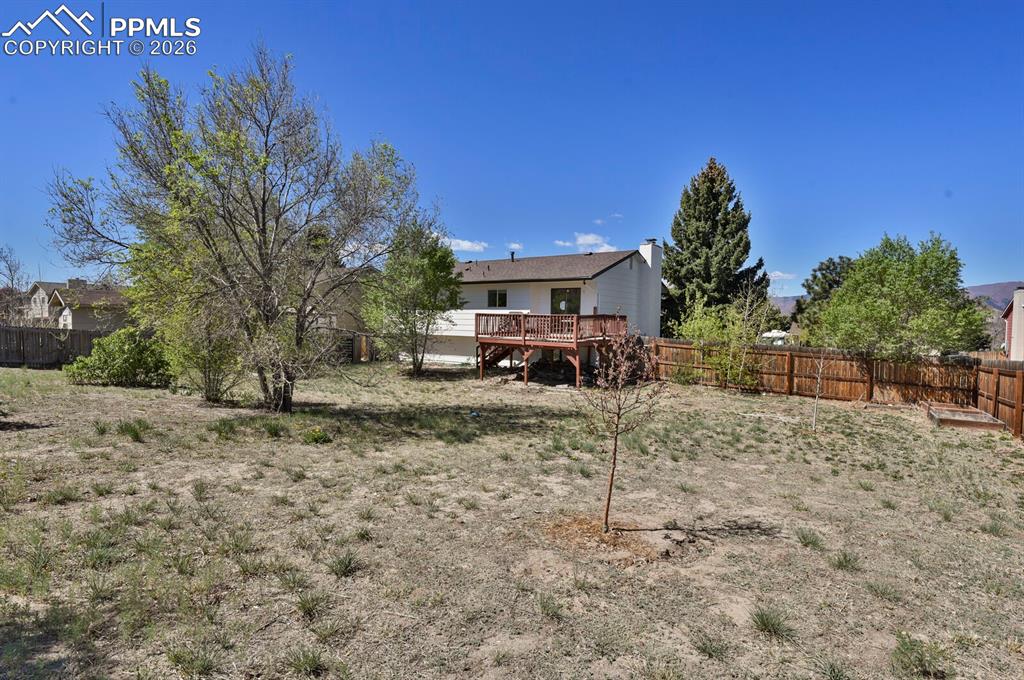 Image 28 of 30: The property features a spacious yard with a deck, mature trees, and a wood