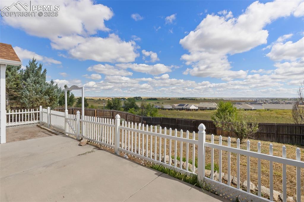 Image 38 of 50: Walk out onto the back patio with a white fence seperating the large backya