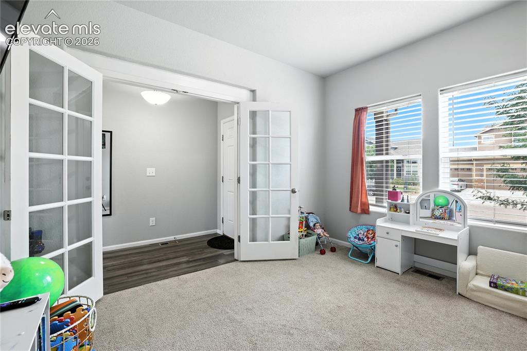Image 13 of 42: French doors with glass panels, light carpet flooring, large windows with b